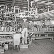 Black and white historical image of workers on product assembly line packaging Oronite products.