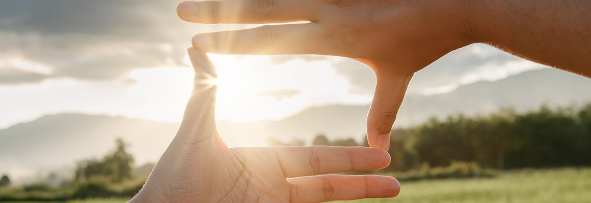 Hands held up in the shape of a rectangle looking out at a beautiful landscape.