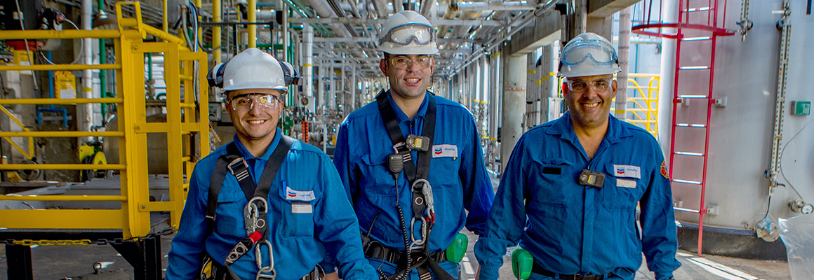 Three male workers smiling as they walk towards camera at a Chevron Oronite plant.