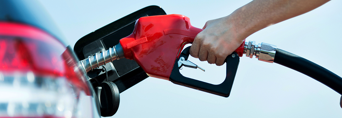 Hand on gas pump nozzle pumping fuel into vehicle.