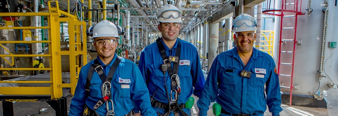 Three male workers smiling as they walk towards camera at a Chevron Oronite plant.
