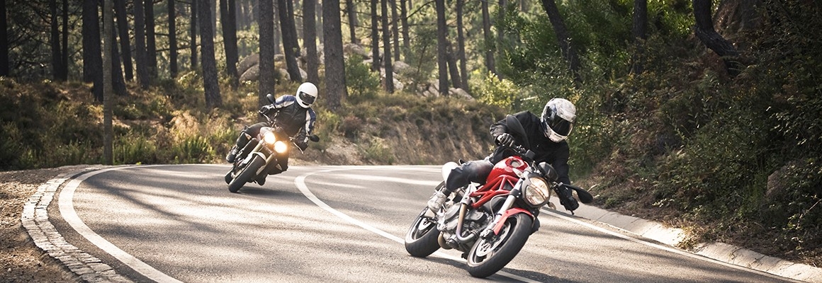 Two people riding motorcycles around a turn in the road.